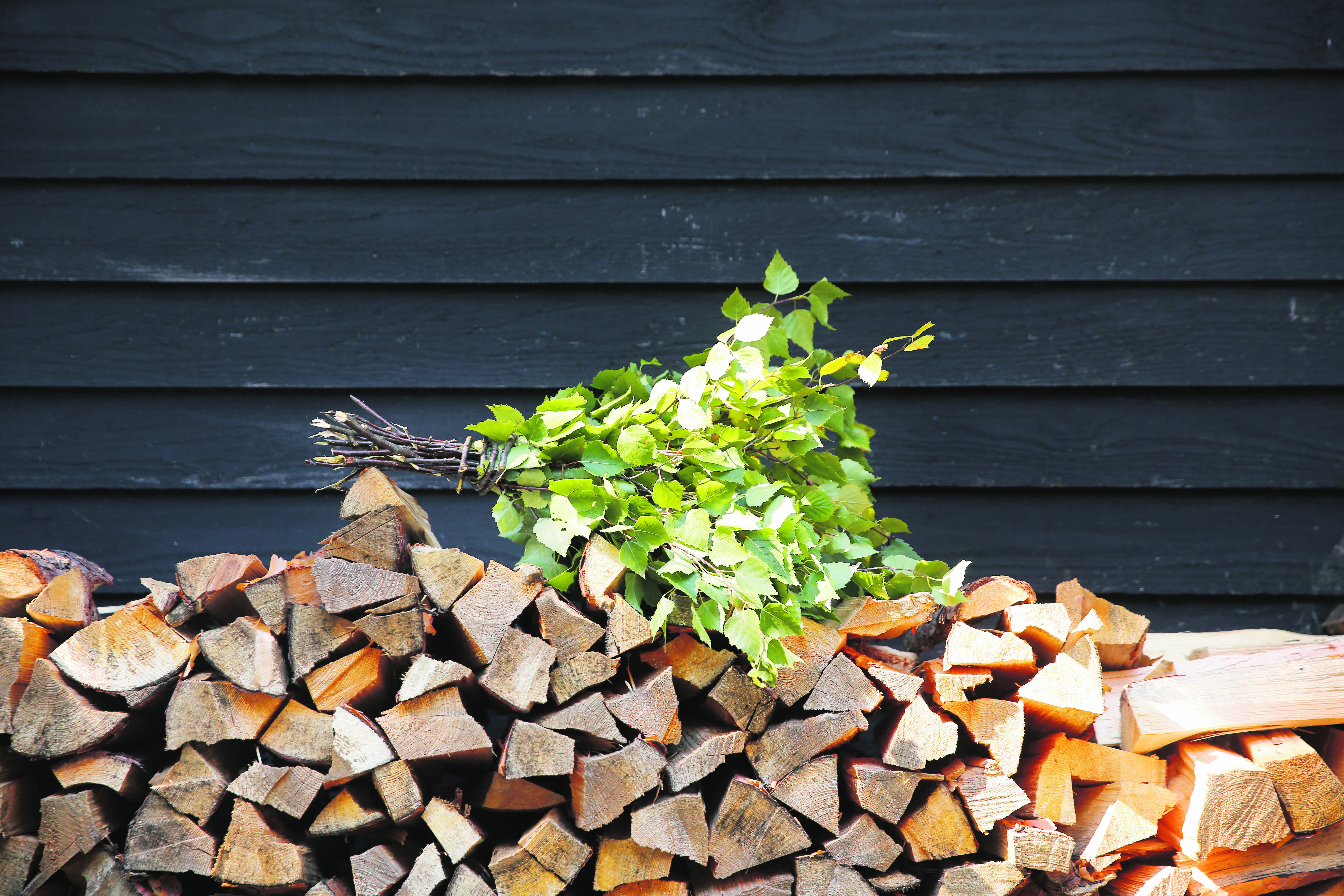 Auf einem Stapel Brennholz an der Außenwand einer hölzernen Sauna in Finnland liegt eine Birkenquaste