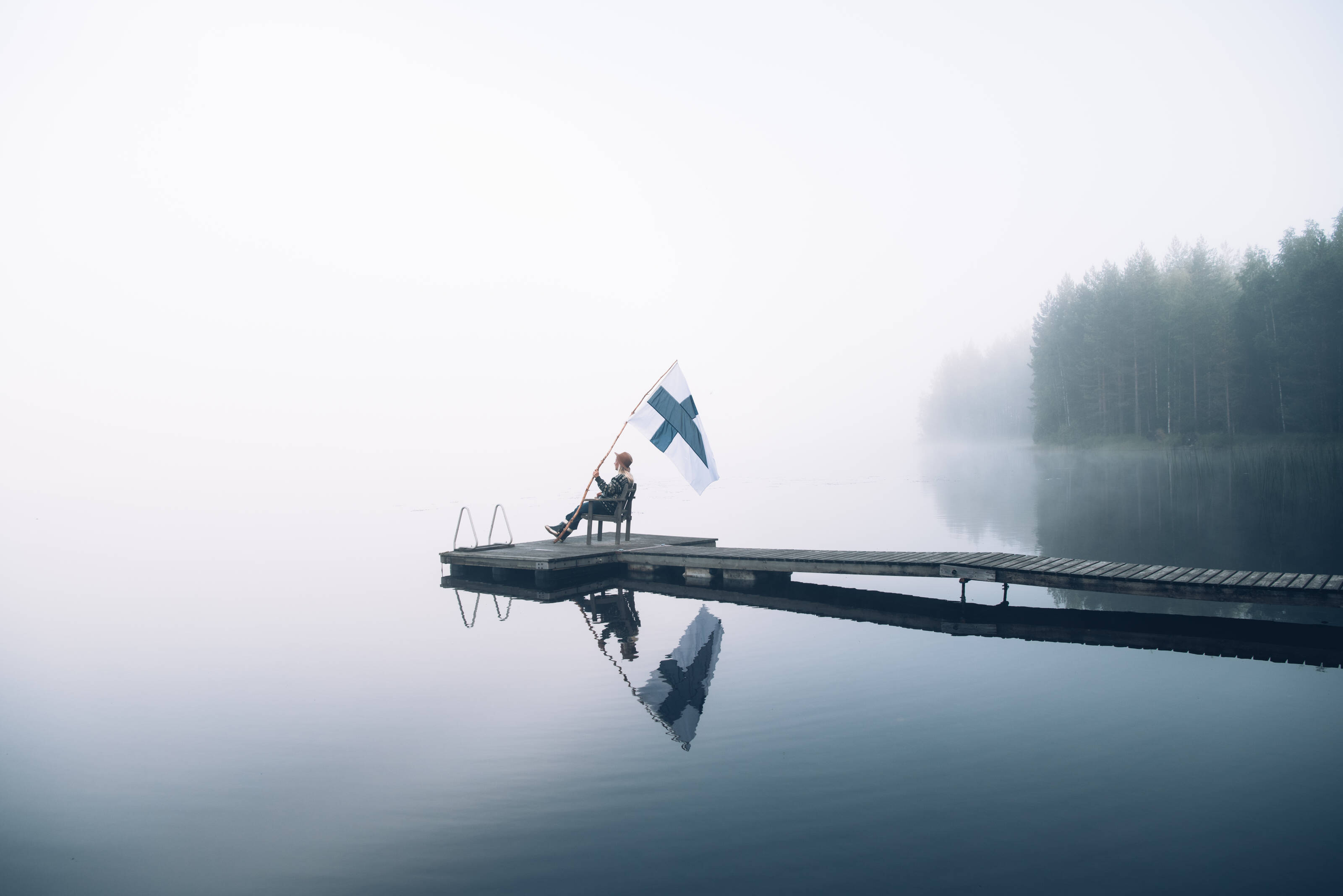 Person sitzt am See mit der finnischen Flagge.