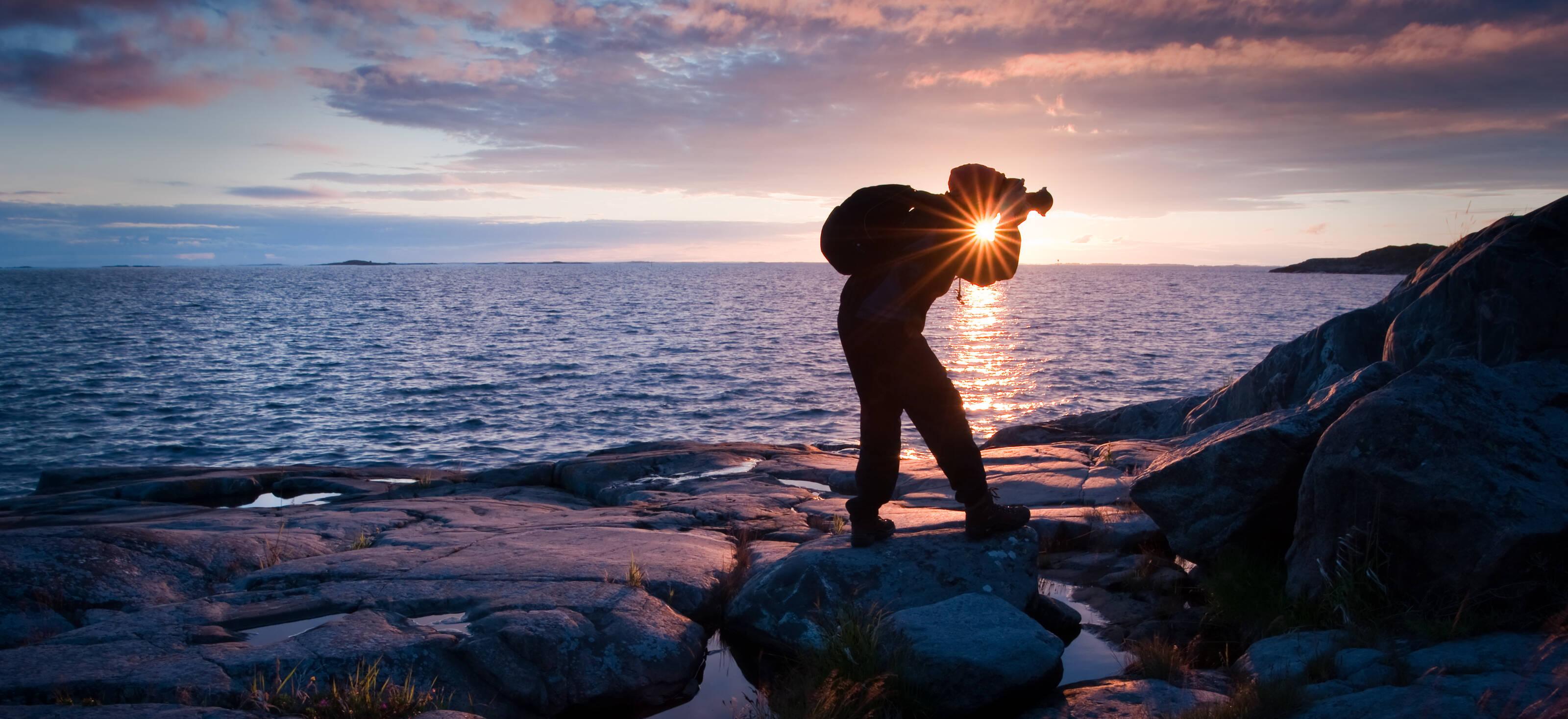 Ein Mann fotografiert die Küste bei Sonnenuntergang.