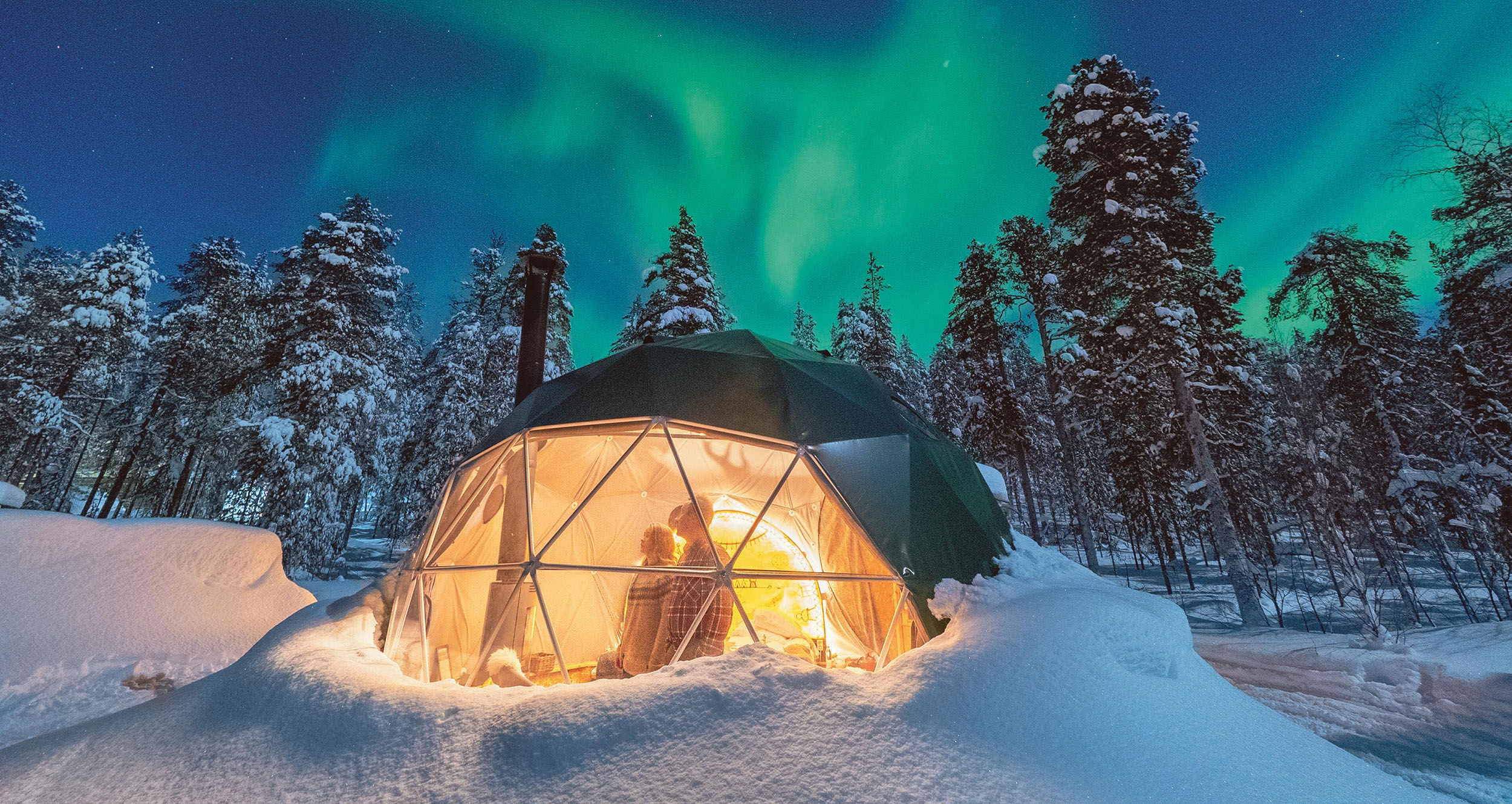 Menschen beobachten das Nordlicht in einer Aurora-Kuppel.