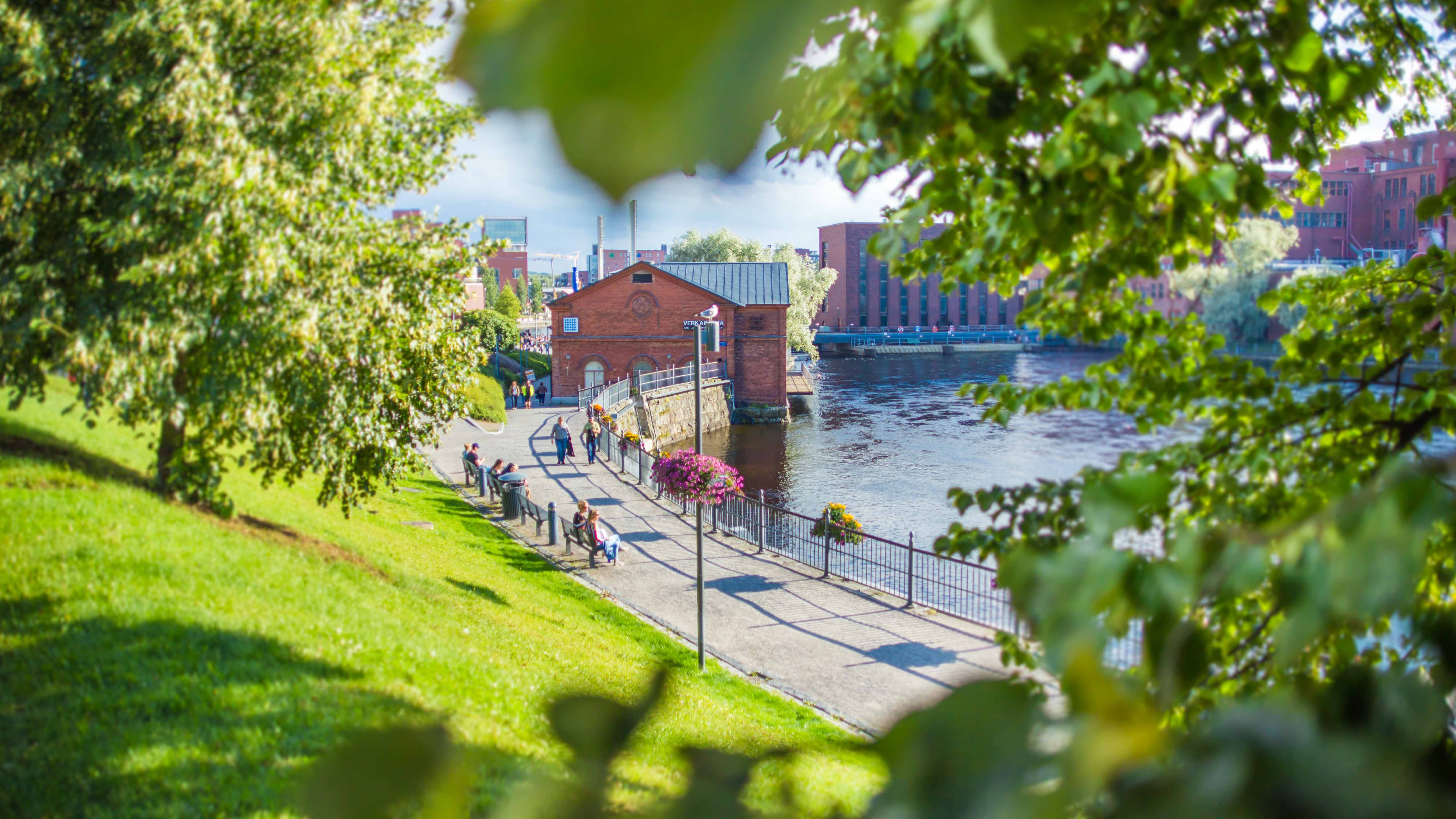 Ein sonniger Park voller Menschen am Ufer der Tammerkoski-Stromschnellen in Tampere