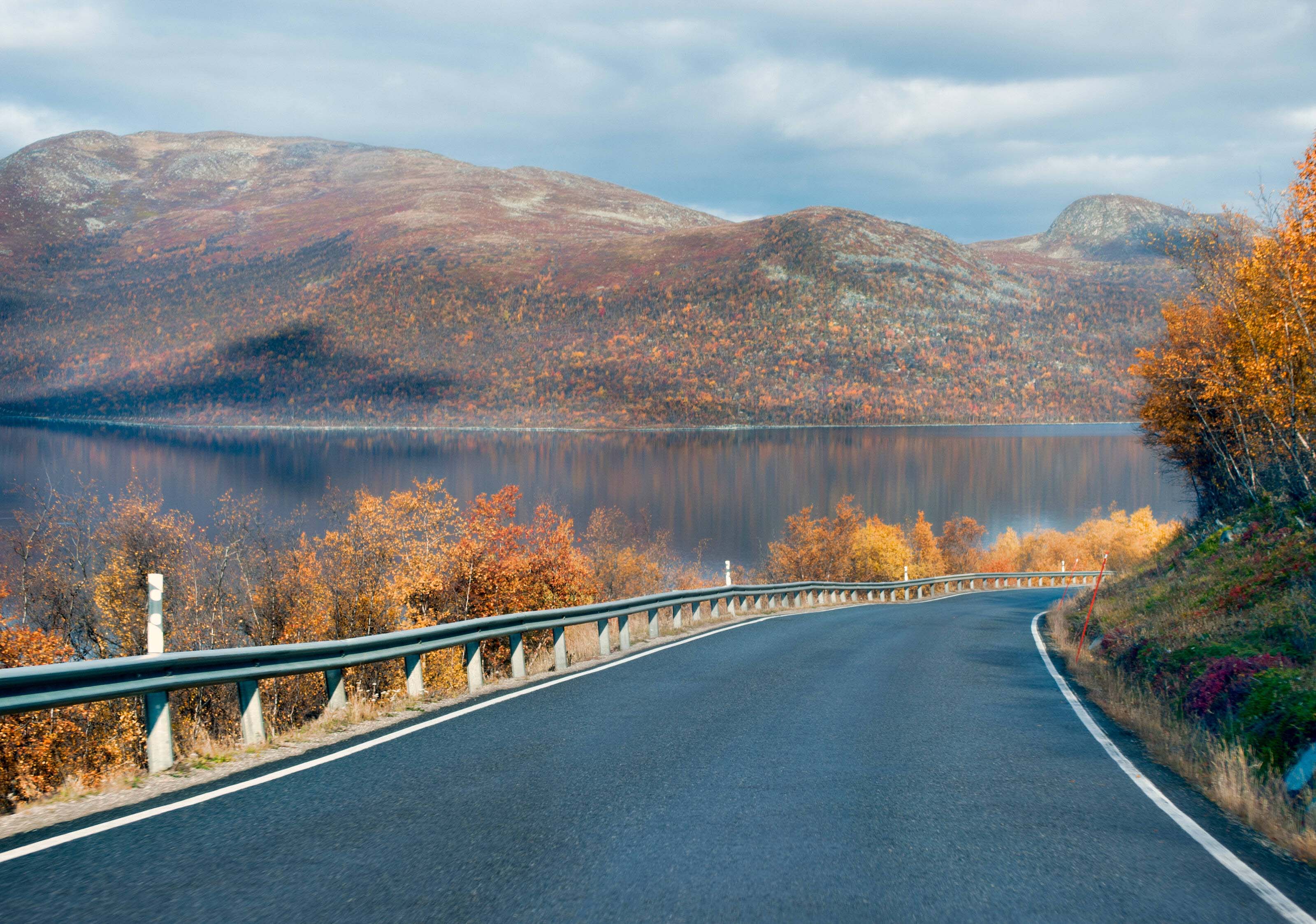 Eine von oben fotografierte gerade Asphaltstraße, die eine verschneite Waldlandschaft in Lappland durchquert